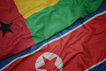 waving colorful flag of north korea and national flag of guinea bissau.
