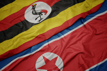 waving colorful flag of north korea and national flag of uganda.