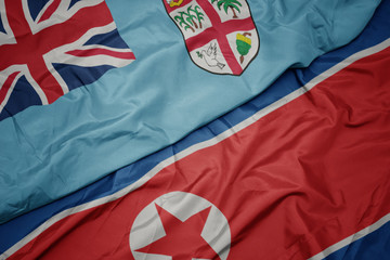 waving colorful flag of north korea and national flag of Fiji .