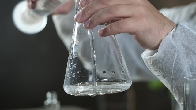 scientist in chemical laboratory pours clear solution from test tube into beaker. specialist makes scientific Experiment in biochemistry. pharmaceutical research and development concept.