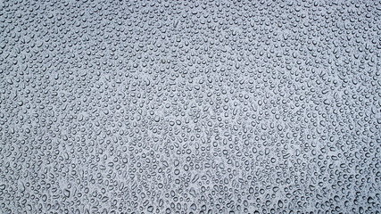 Pattern of chaotically arranged drops of water in the morning passed the day before rain or dew on the metal front hood of a bluish gray car.