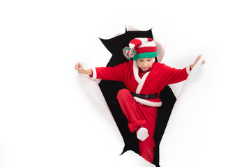 Child Santa Claus comes out of a hole in paper. A boy in a New Year's costume is smiling. Holiday surprise. Christmas holiday concept