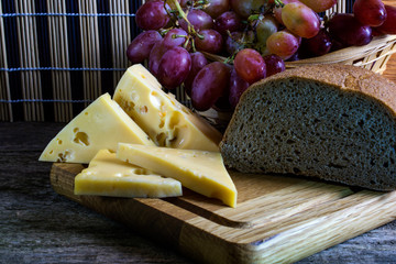 Cheese, grapes in a wicker basket, bread lies on a cutting board.
