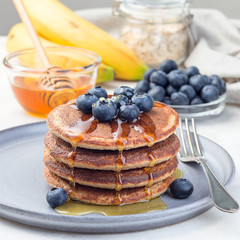 Healthy oatmeal banana pancakes garnished with blueberry and honey, on  gray plate, square format