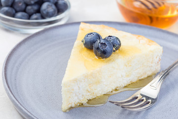 Piece of cheese casserole or cheesecake, garnished with blueberry and honey, on a gray plate, horizontal