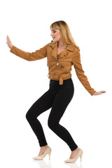 Carefree Young Woman In Brown Suede Jacket Is Dancing With Arms Outstretched.