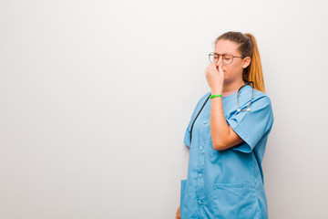 young latin nurse feeling disgusted, holding nose to avoid smelling a foul and unpleasant stench...