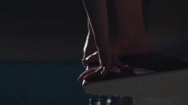 Close up shot in slow motion of a professional female swimmer's feet preparing to jump off the starting block into the swimming pool. Night shot