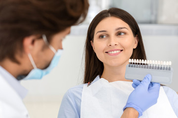 Dentist putting sample from tooth scale to smiling woman
