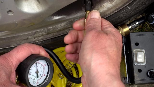 Close up of a man&rsquo;s hand screwing the connection of a tyre / tire inflator to a valve, and switching on the pump while holding the pressure gauge.