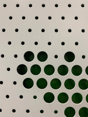 Close up view of white metal surface with green color background. Dotted graphic pattern is cut out.