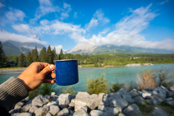 Selective focus of a persons hand holding a blue cup of tea or coffee with in the background a...