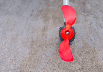 Bright orange propeller, part of an electric outboard motor, beach sand background.