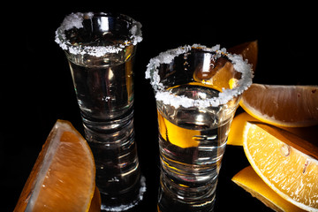 Two tequila shots with lemon and salt with reflection on shiny black background