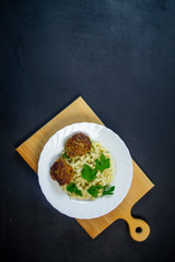 boiled pasta with meatballs on a white plate on a wooden board