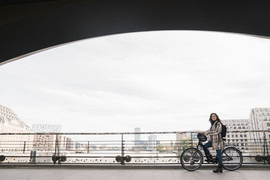 Woman with a bicycle standing on a bridge in the city, Berlin, Germany