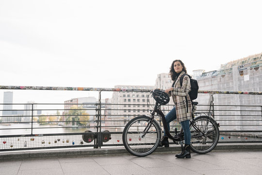 Woman with a bicycle standing on a bridge in the city, Berlin, Germany