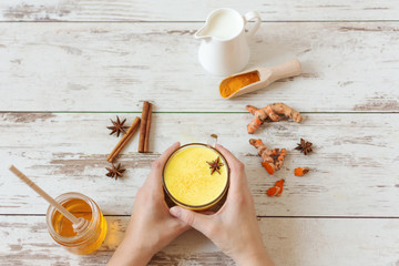 Woman hand holding a golden turmeric milk with cinnamon and other aromatic spices top view. Healthy...