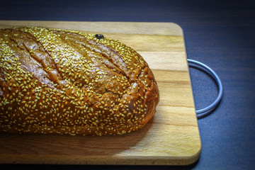 On a wooden Board lies a fresh black bread with sesame seeds