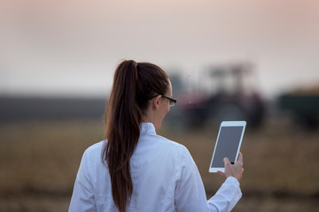 Woman agronomist with tablet in front of tractor in field