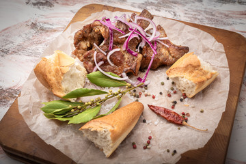 Still life food on a bright colorful table on a cutting Board on crumpled baking paper baked meat sprinkled with onions red Bombay with spices a sprig of Bay leaf and a French bun baguette