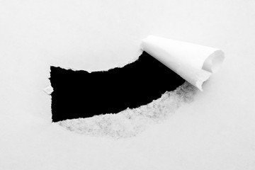 A hole in white paper with torn edges and a black isolated background inside.