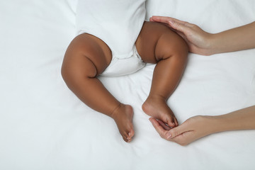 American baby girl lying on white bed with mother hands