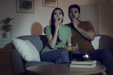 Emotional young couple watching movie using video projector at home