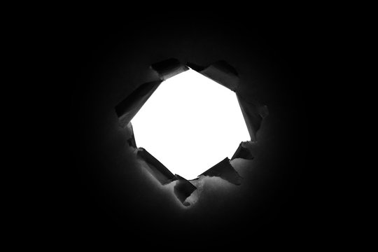 A round hole in black paper with torn edges isolated with a white isolated background inside.