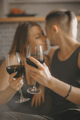 Romantic couple looking at each other smiling ang holding glasses with red wine. Pleasant day with lovely people at home.