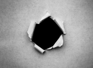 A hole in vintage paper with torn edges close-up with a black isolated background inside.