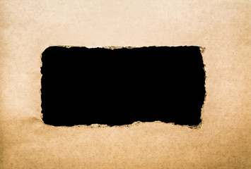 A hole in vintage paper with torn edges closeup and a black isolated background inside.