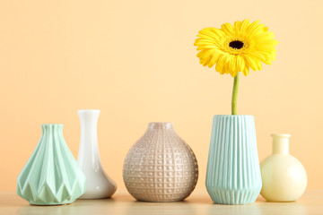 Different ceramic vases and gerbera flower on beige background