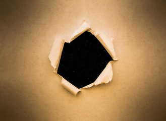 A hole in vintage paper with torn edges close-up with a black background inside with colorful space stars in the universe.