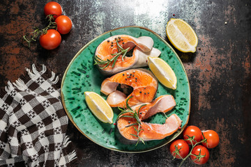 Raw steaks of wild salmon with lemons, tomatoes and spices on the plate top view. Sea food concept.