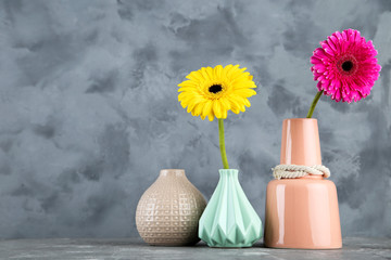 Different ceramic vases with gerbera flowers on grey background