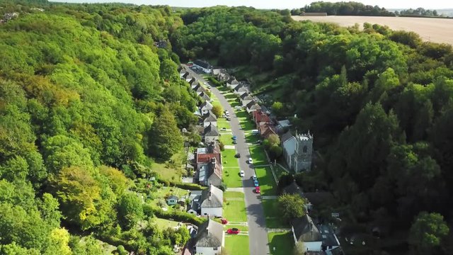 Quiet little town street with houses on both sides between a forest - drone rising