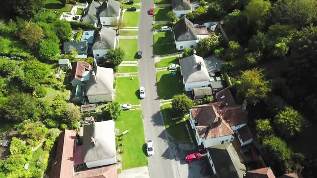 Quiet little town street with houses on both sides between a forest - aerial pan shot