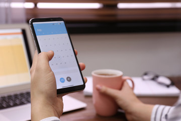 Woman holding smartphone with calendar app at table, closeup
