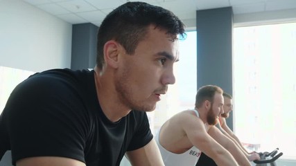 Focused sporty men cycling on spin bikes in gym. Athletic muscular men in sportswear training in cycling class