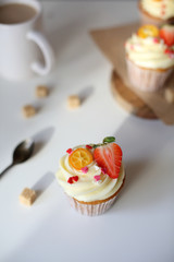 cupcake with cream cheese decorated with strawberries on a white background.