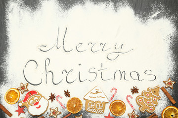 Text Merry Christmas on flour with gingerbread cookies, dry oranges and candies