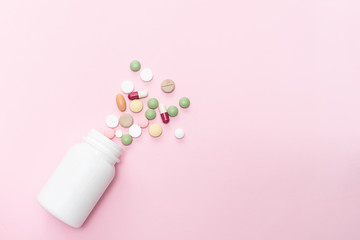 Flat lay overhead of different medical tablets, pills and capsules and white plastic bottle on pink pastel background with copy space for your text. Health care concept.