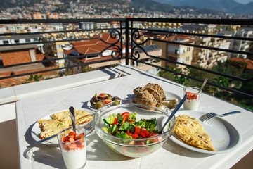 Healthy breakfast on balcony. Whole grain bread with pumpkin seeds and cheese. Salad from fresh cucumbers and tomatoes. Fresh figs. Strawberries with yogurt. Direct sun light. Alanya, Turkey.