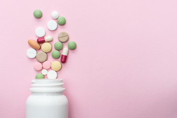 Flat lay overhead of colorful drugs and pills and white plastic bottle on pink pastel background with copy space for your text. Health care concept. Template medical blog social media.