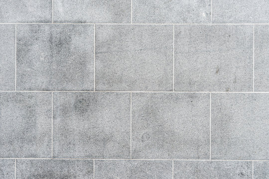 Texture of gray road granite tiles with white seams. Stone background.