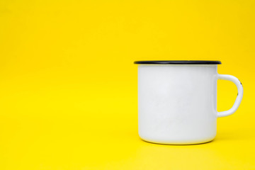 Enamel white metal mug with black line on the edge on yellow background. Mug empty blank for coffee or tea. Space for text