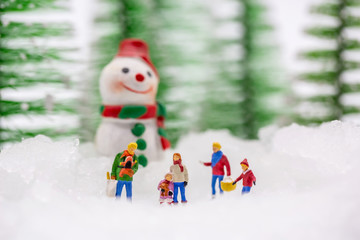 Happy snowman on snow with background of blurred Christmas pine. Miniature people in Christmas...
