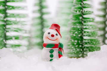 Happy snowman on snow with background of blurred Christmas pine. Miniature people in Christmas Theme.