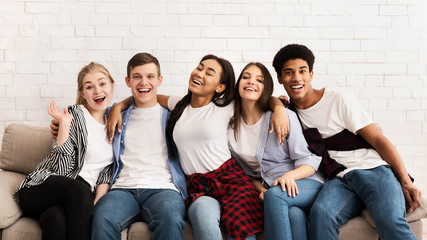 Teen friends sitting on sofa and embracing, smiling to camera